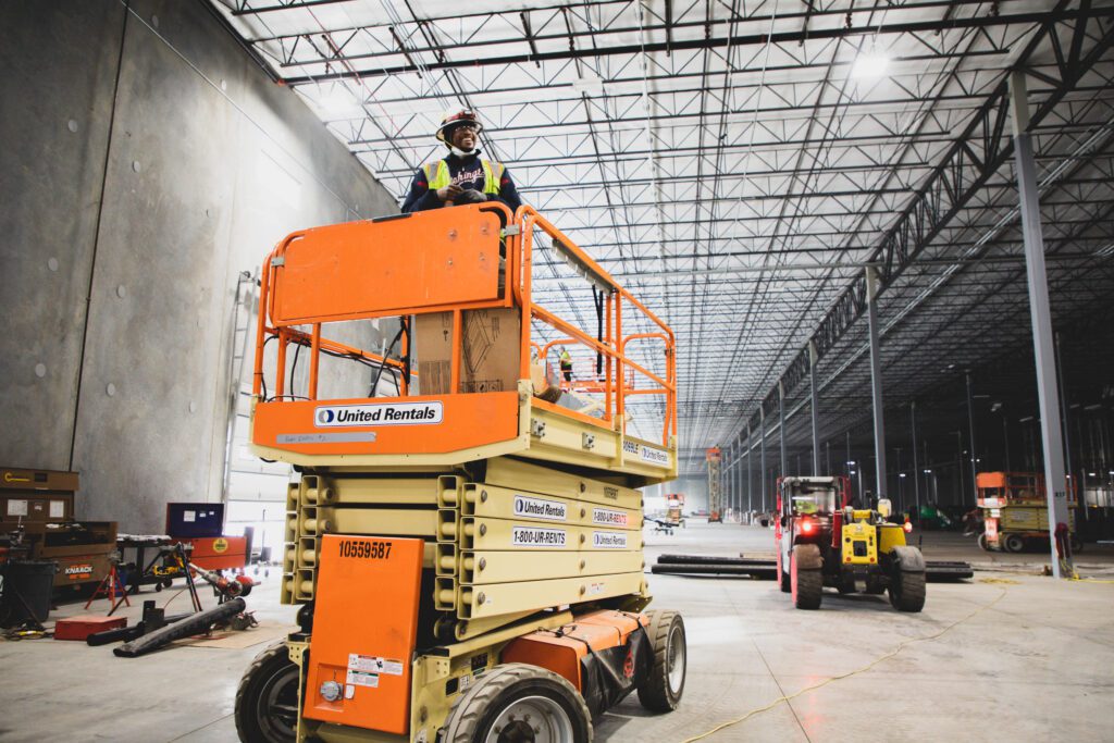Electrician standing on commercial lift in a large warehouse.
