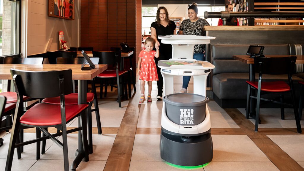 self serving robot inside a restaurant with a family in the background