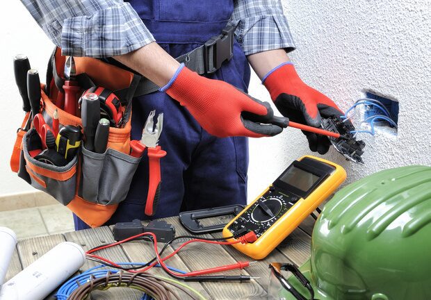 Electrician with red gloves cutting wires with a handy kit around his belt and a circut tester right below him