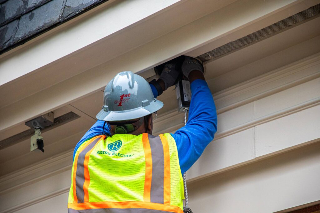 electrician working on the ceiling of a building wearing a 1st safety hard hat and a Rogers Electric safety vest