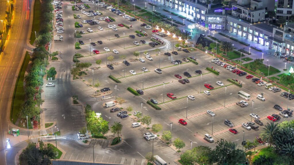 Nighttime aerial view of a lot of cars in illuminated parking with green trees near highway timelapse in Business Bay, Dubai, United Arab Emirates