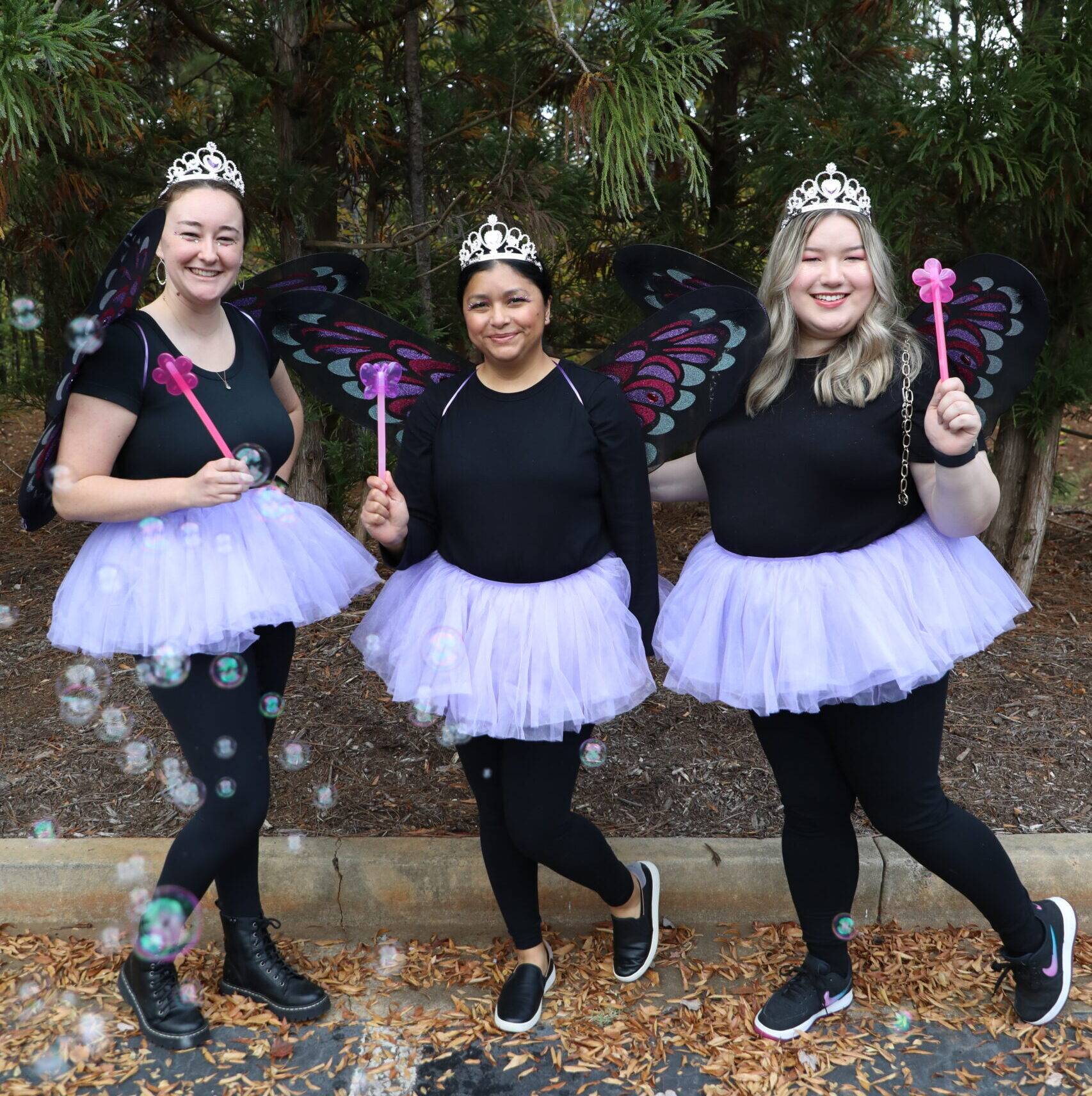 3 women dressed as fairies with flower wands, crowns, and wings