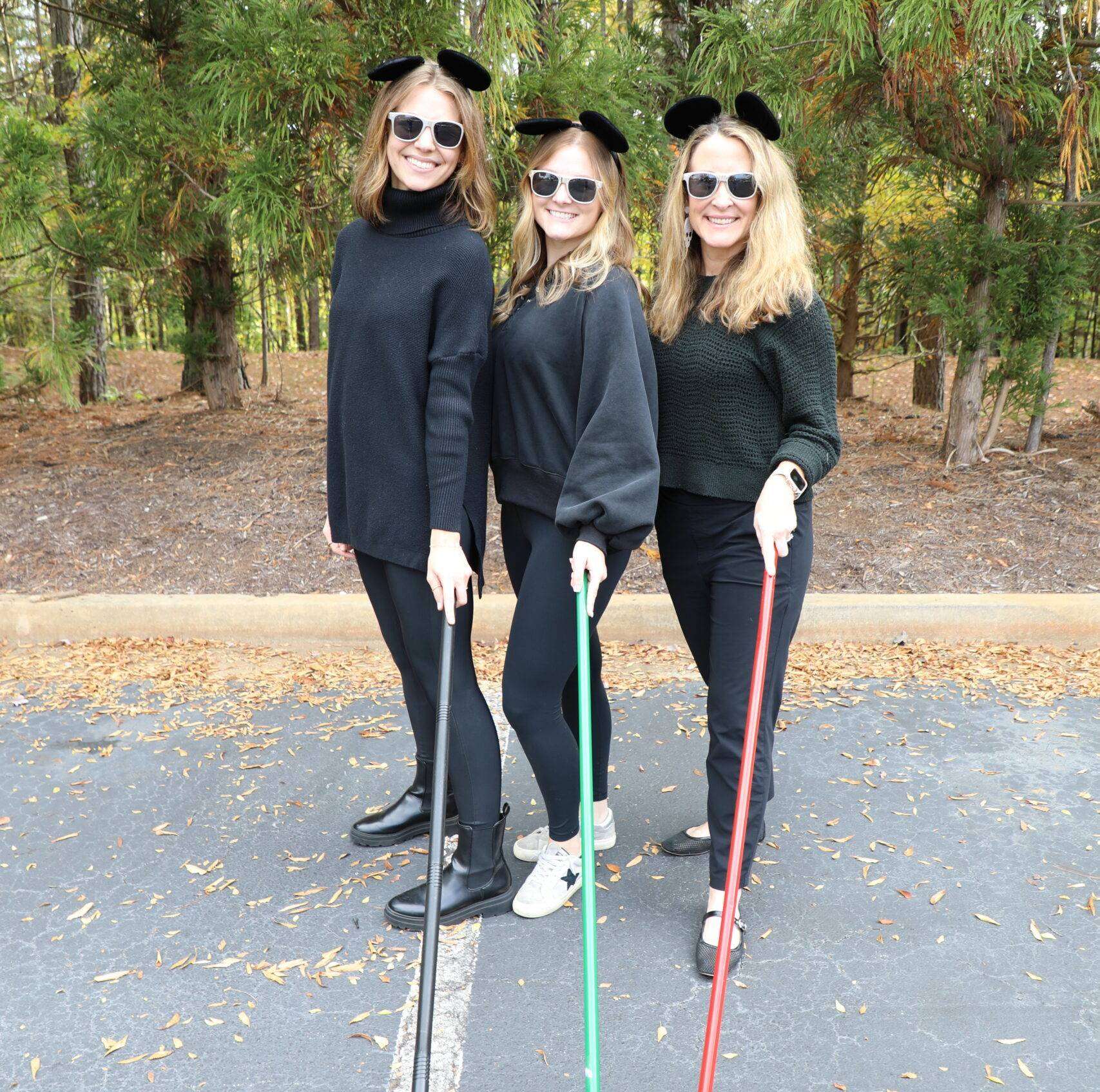 3 Women with sunglasses, sticks, and ears all dressed in black