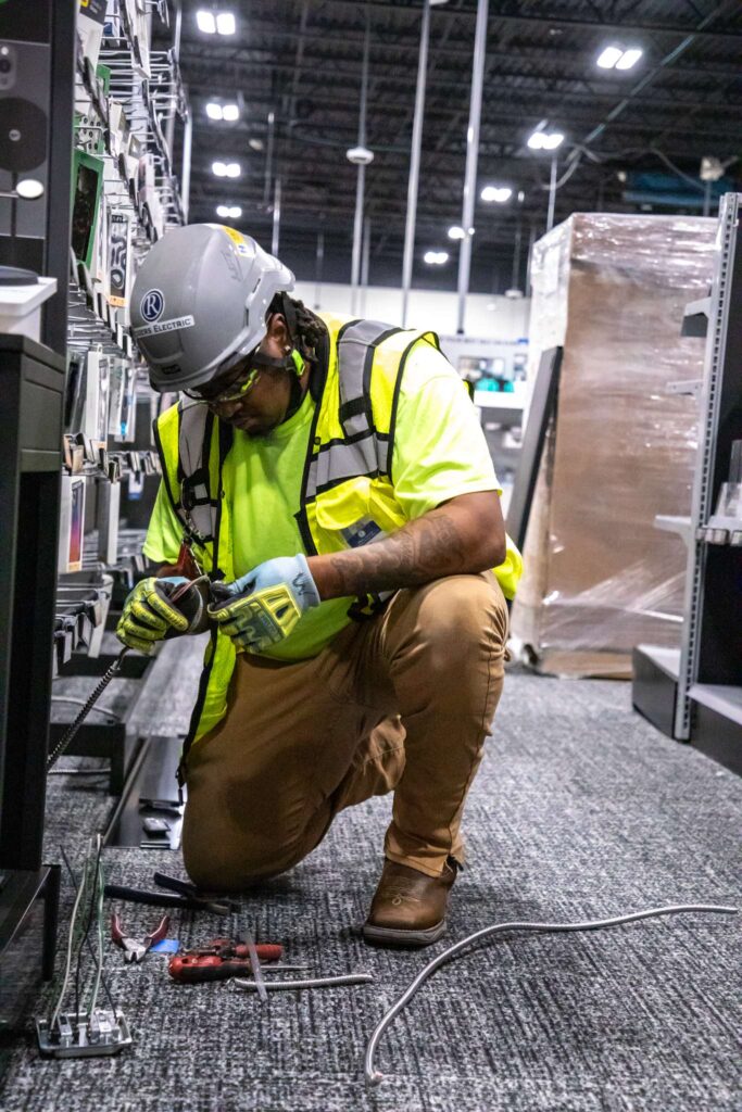 electrician in a retail store on knees working on wires and outlets with full PPE gear on