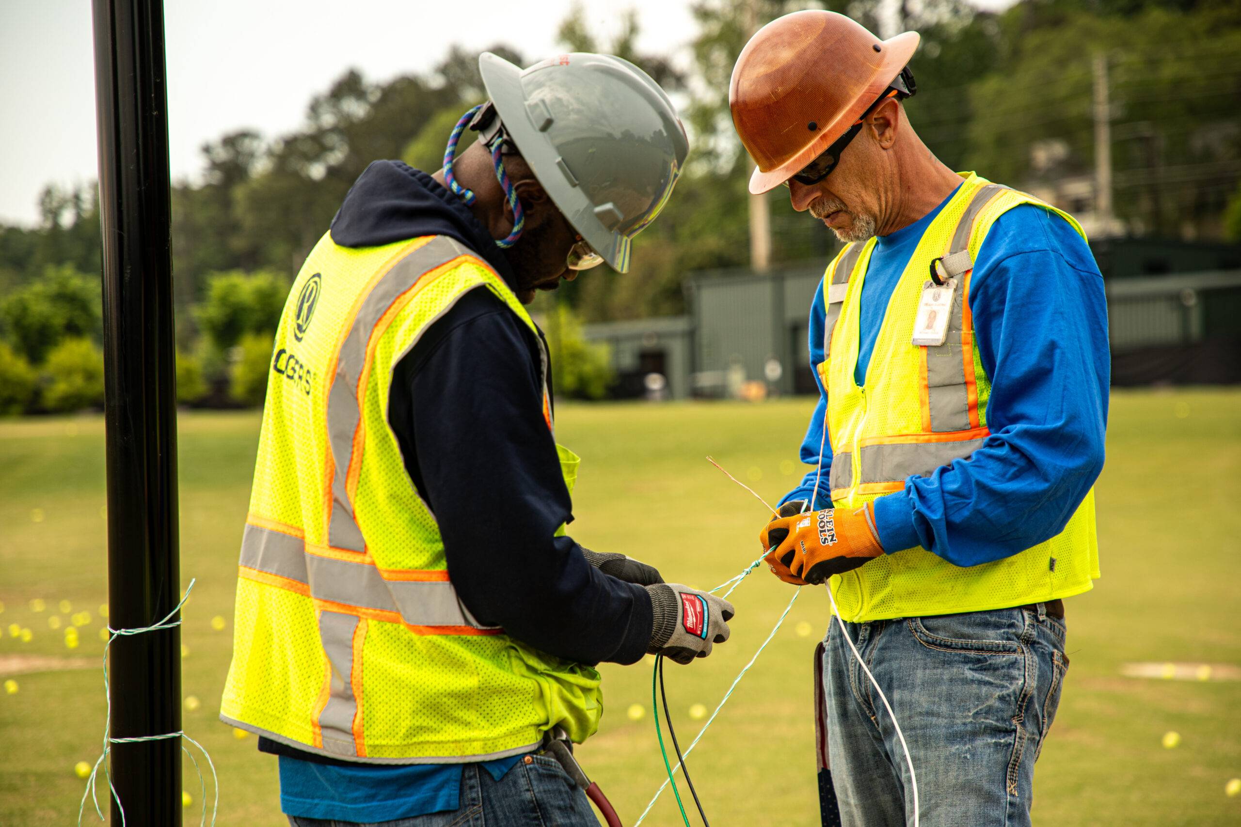 two electricians braiding cable together on a golf course wearing full Rogers Electric PPE gear