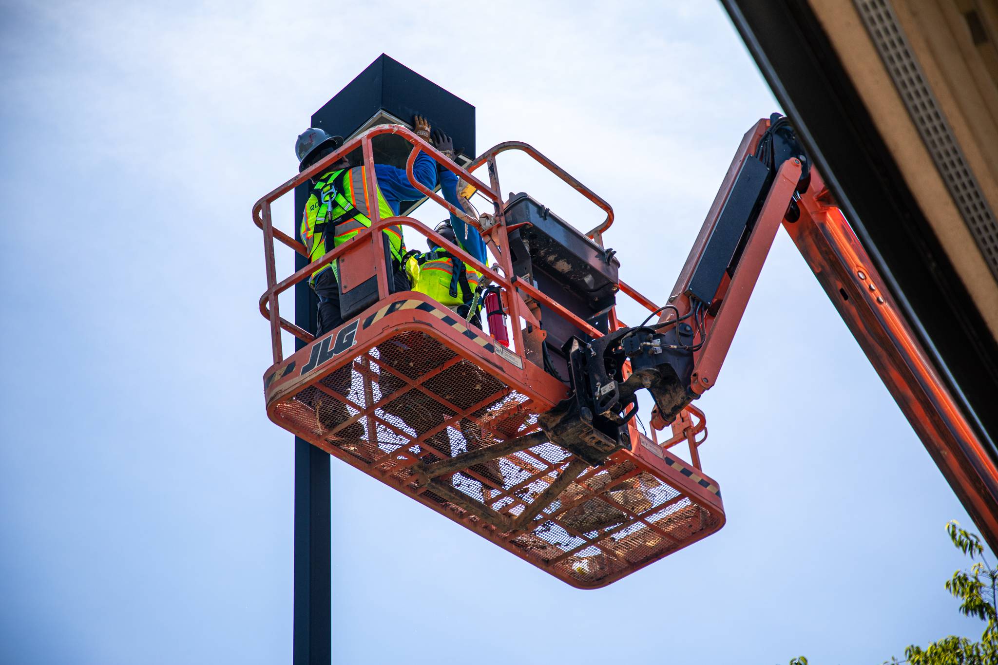 Two electricians in a scissor lift working on parking lot lighting