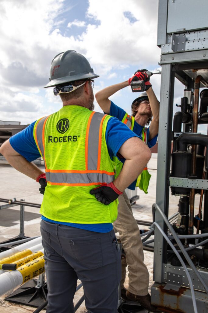 two Rogers Electric electricians with PPE gear on drilling 