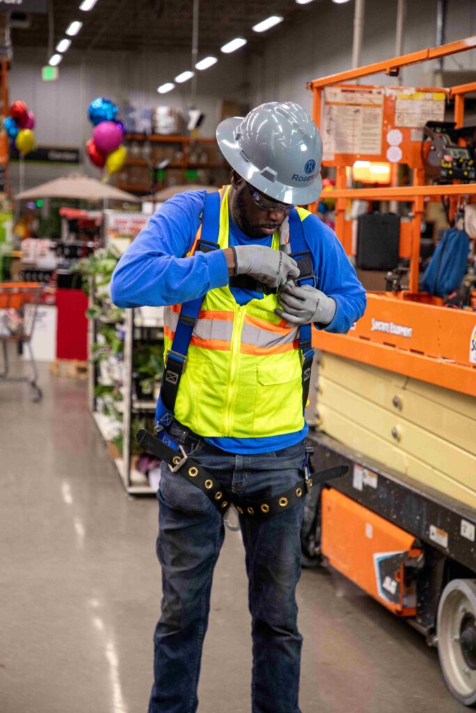 electrician inside of a home retail store putting on a scissor lift harness with full PPE gear on 