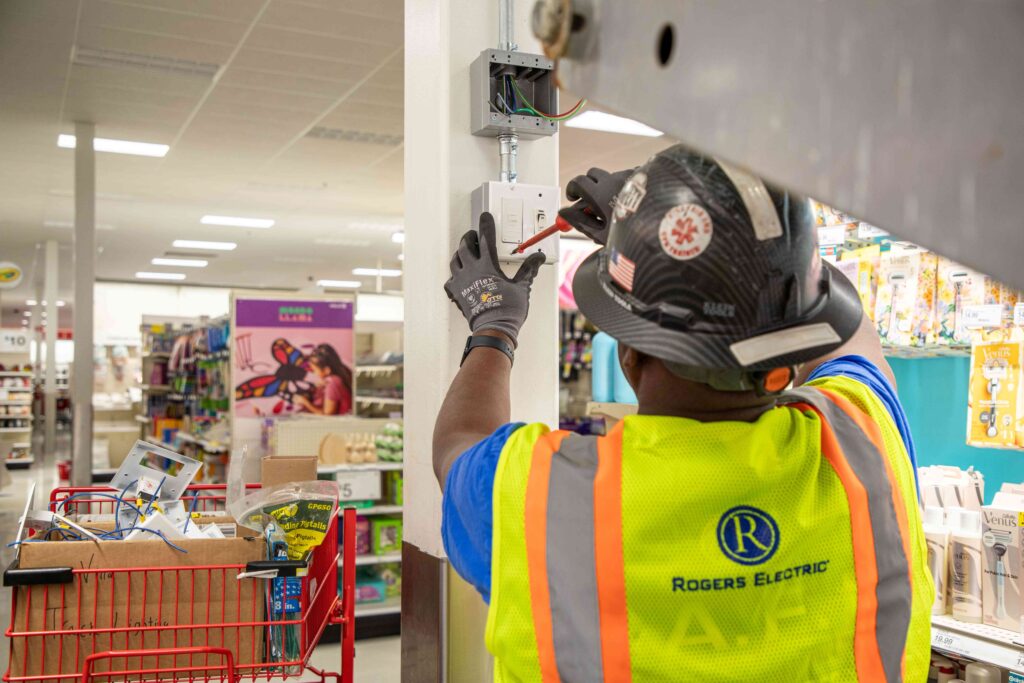 the backside of a Rogers Electric electrician wearing full ppe gear installing an outlet into a retail store pole