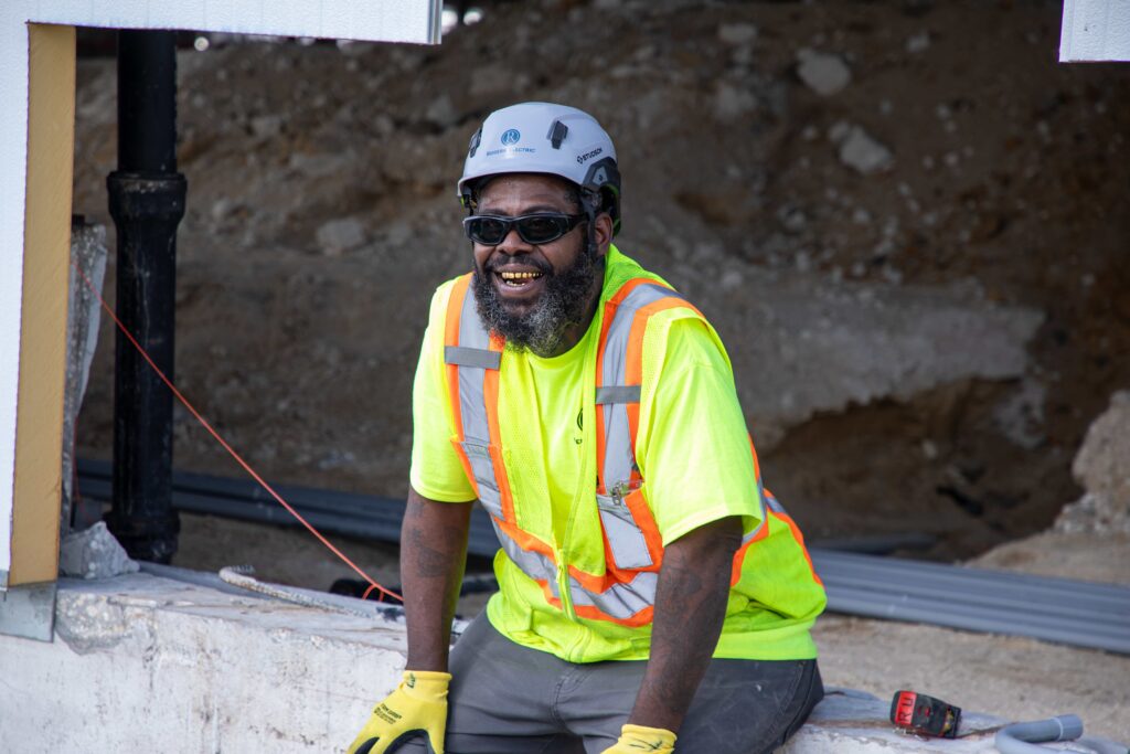 a Rogers Electric construction electrician in full ppe gear sitting down and smiling