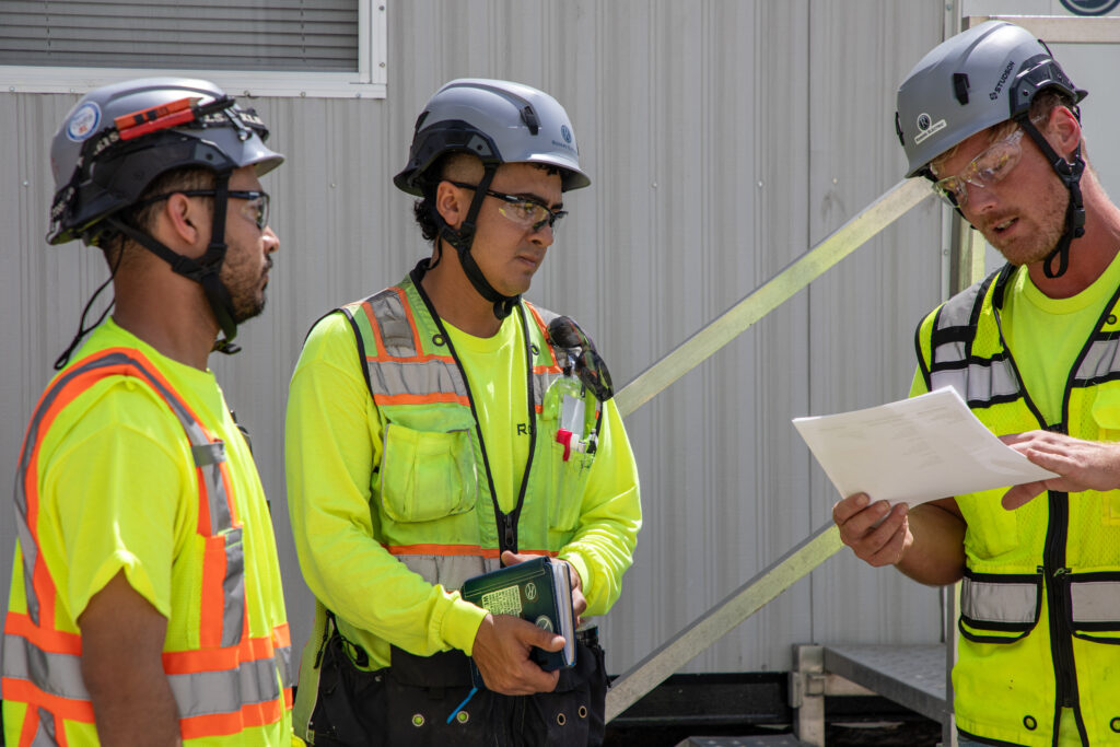 3 Rogers Electric construction electricians talking while looking over some paperwork