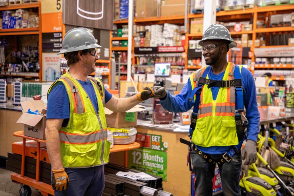 picture of two Rogers Electric electricians wearing full PPE gear in a home retail store smiling and giving a fist bump to each other