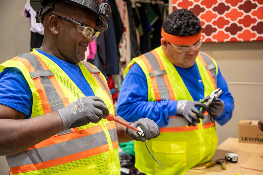 Two commercial electricians working in a retail store holding tools.