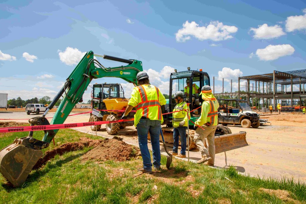 Three construction workers standing over a ditch on a jobsite.