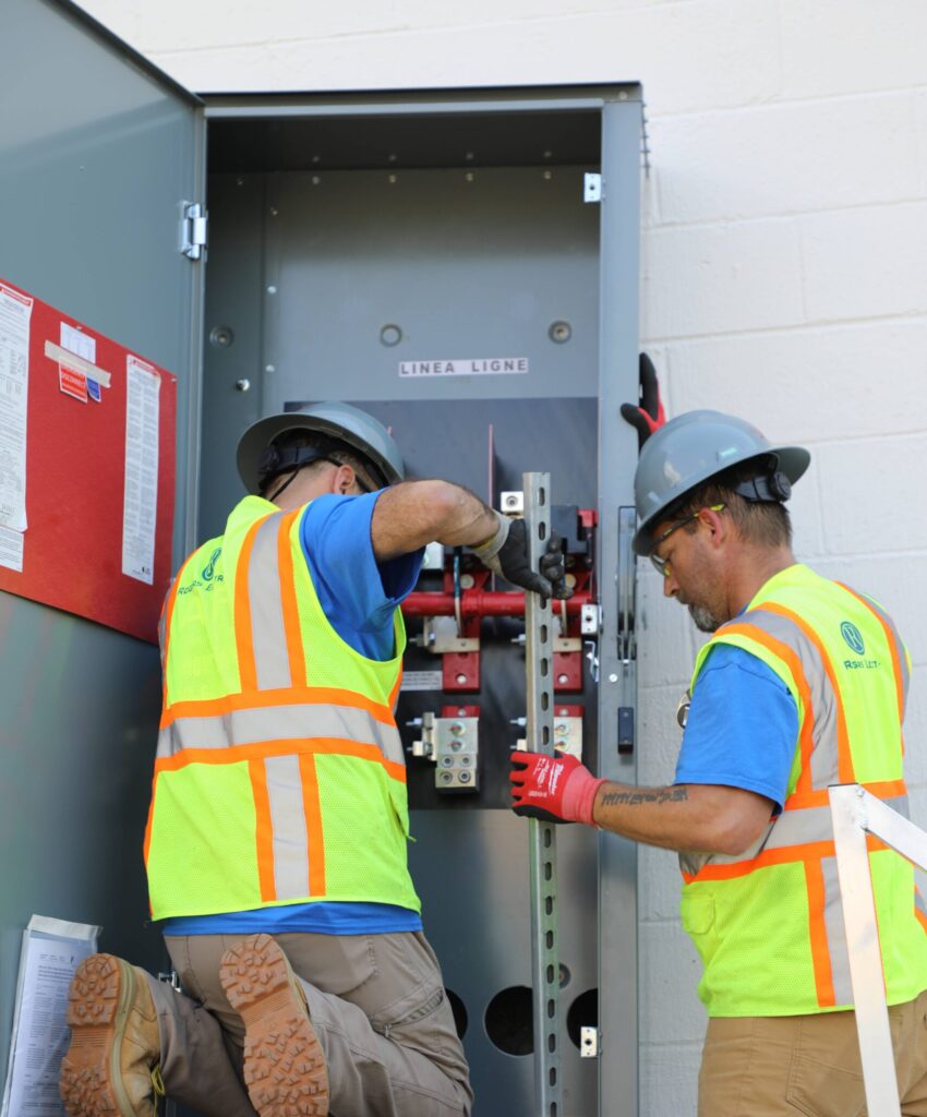Two commercial electricians working on an electrical panel.