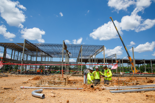 Three commercial electricians working in the field looking at blueprints in a ditch for wiring.