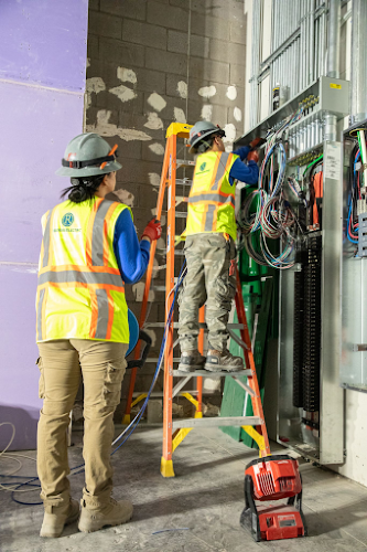 Two commercial electricians working on a jobsite. One is on a ladder.