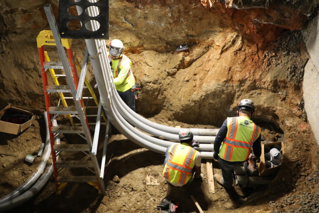 Three commercial electricians in an underground ditch working on pipes.