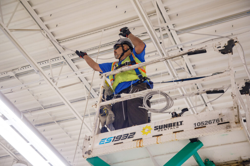 Electrician installing electrical wiring from scissor lift during commercial lighting upgrade.