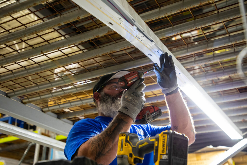 Electrician installing an energy-efficient LED lighting system in a commercial facility to reduce power usage and qualify for utility rebates.