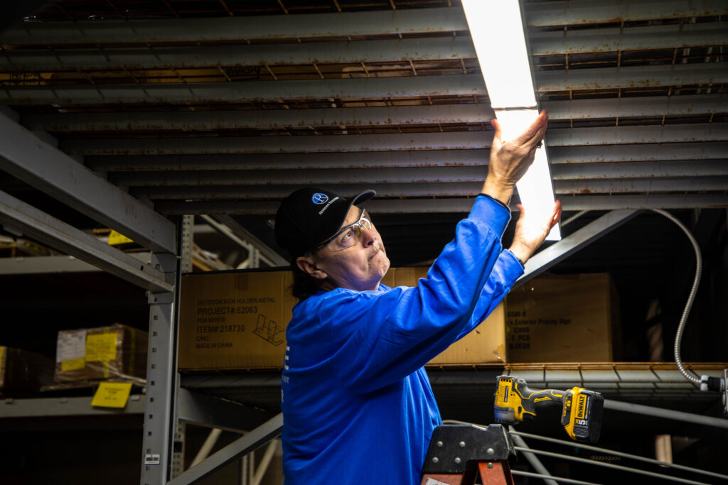 Technician installing LED lighting in a warehouse to improve visibility, increase energy efficiency, and support commercial lighting rebate incentives.