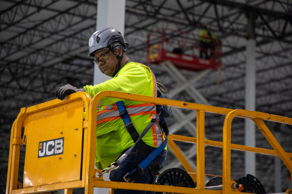 Electrician working inside a large-scale data center construction project using elevated equipment and full PPE during infrastructure installation.